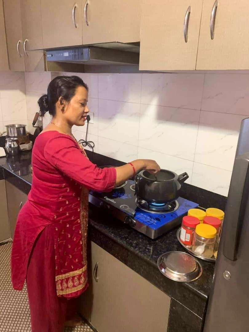 Eine Frau kocht in einer Küche. Sie trägt die typische Kleidung in Nepal, einen roten Sari über einer roten Hose.