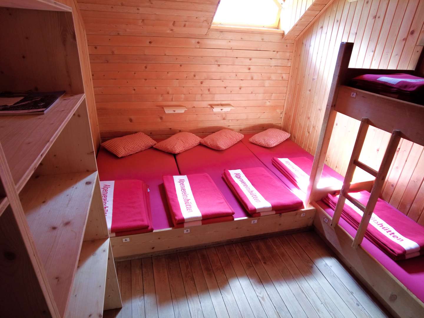 Ein Zimmer mit einem Matratzenlager, das mit roter Bettwäsche bezogen ist. An der Seite steht ein Hochbett mit demselben Bettenbezug.