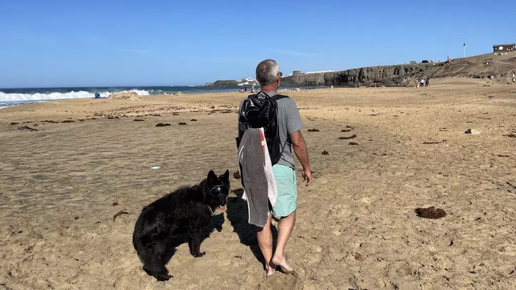 Ein Mann und ein schwarzer Schäferhund auf einem weiten, leeren Strand