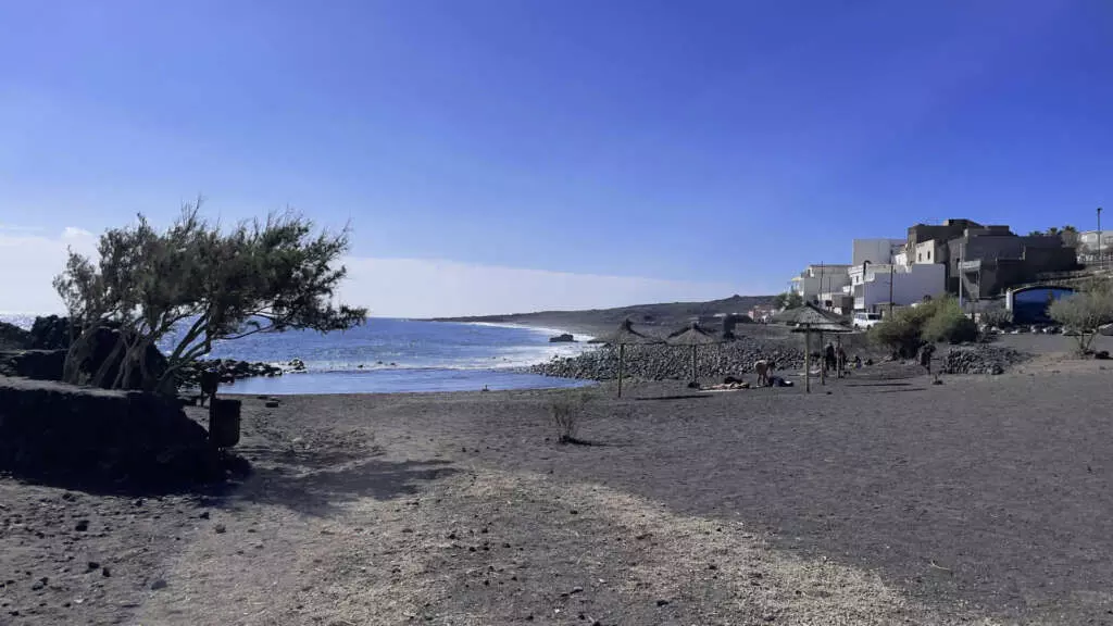 Ein Strand mit schwarzem Sand vor einer kleinen Ansammlung von Häusern